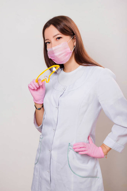 Portrait of a woman in a white coat, mask and gloves holding glasses in her hands. Photo on a white background. - Photo, Image