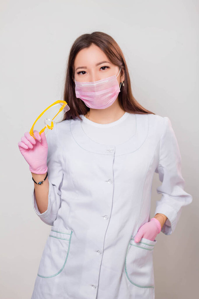 Portrait of a woman in a white coat, mask and gloves holding glasses in her hands. Photo on a white background. - Valokuva, kuva