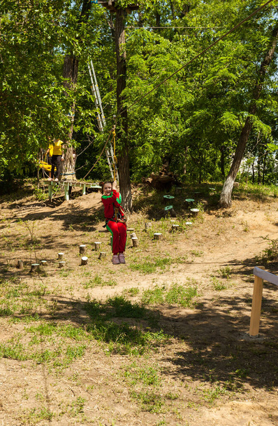 Girl in bright red tracksuit jumping in high rope course enjoying the adventure - Photo, Image