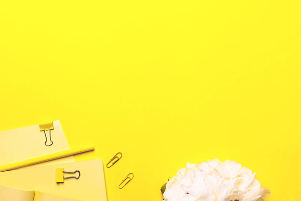 Business concept - Yellow background with opened light yellow fabric notebooks, flowers and paper clips on - 写真・画像