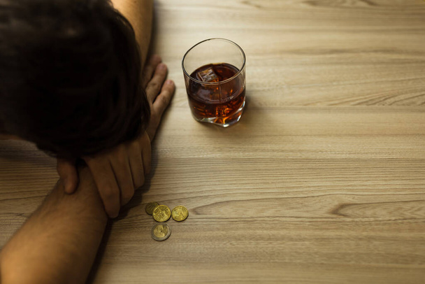 Bunalımlı bir adam, sarhoş, elinde bir bardak konyakla masada uyuyor, şişe ve son bozuk paralarla. Yoksulluk, alkolizm ve depresyon kavramı - Fotoğraf, Görsel