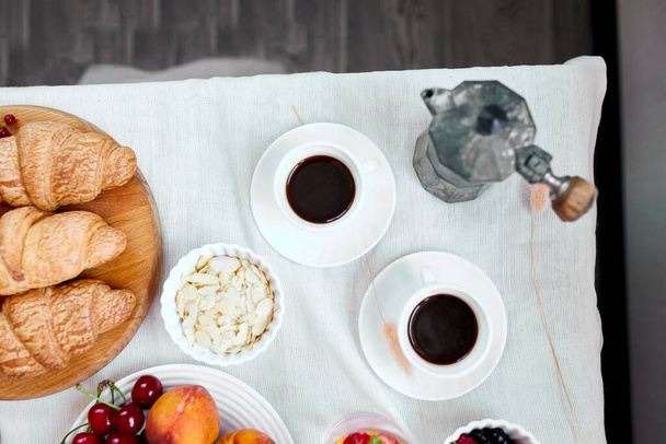 Две чашки кофе и итальянская кофеварка с круассаном и фрукты за столом на дому утром завтрак ритуалы концепции, образ жизни питания - Фото, изображение