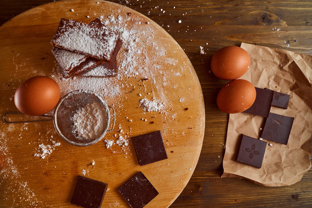 Composition de gâteaux au chocolat empilés sur une table en bois. à côté se trouvent des œufs et des morceaux de chocolat. Vue de dessus. Photo de haute qualité - Photo, image