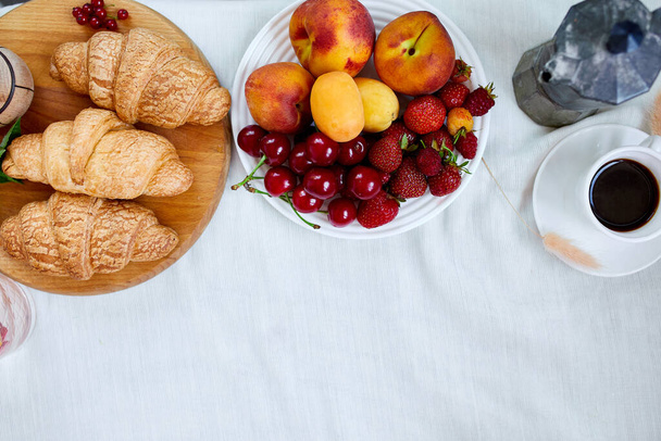 Two coffee cups and Italian coffee maker with croissant and fruits over table at home morning breakfast rituals concept, lifestyle food background - Фото, изображение