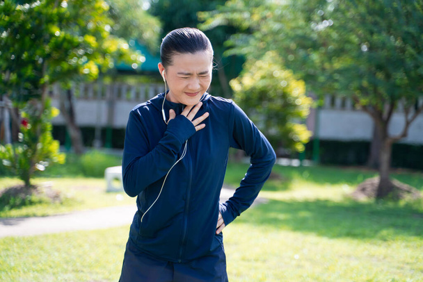 Portrait of Asian woman wearing earphones listening to music was sick with fever at park. Woman exercise at park suffering from sore throat. - Fotoğraf, Görsel