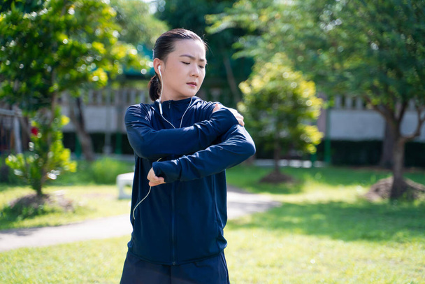 Portrait of Asian woman wearing earphones listening to music was sick with body pain at park. Woman exercise at park suffering from body pain. - Fotoğraf, Görsel