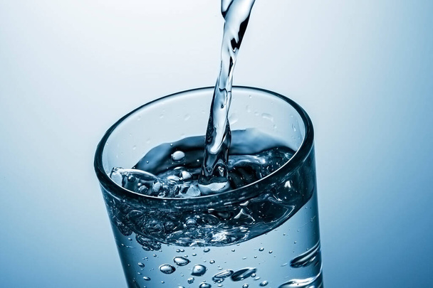 Giet een hoog glas sprankelend water met spetters en bruisende belletjes in een close-up zijaanzicht - Foto, afbeelding