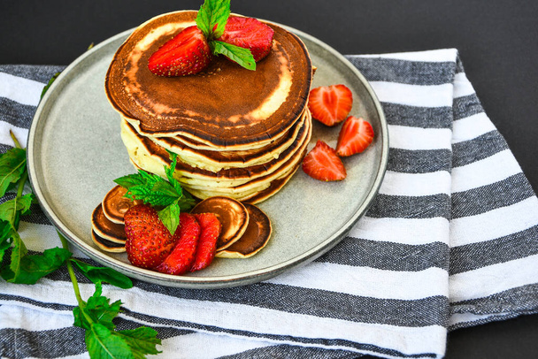 Plate with Traditional Pancakes and Tiny Pancake Cereal with Strawberries and Mint Leaves on a Dark Background. Trendy food. Mini cereal pancakes - Photo, Image