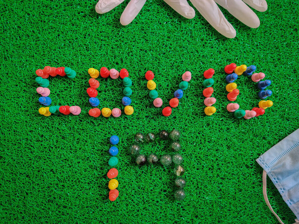 Надпись Covid-19 текст, сделанный с игровой доски штук. Медицинские перчатки, маска, дезинфицирующие средства. Изолированный на зеленом фоне. Медицинская концепция
 - Фото, изображение