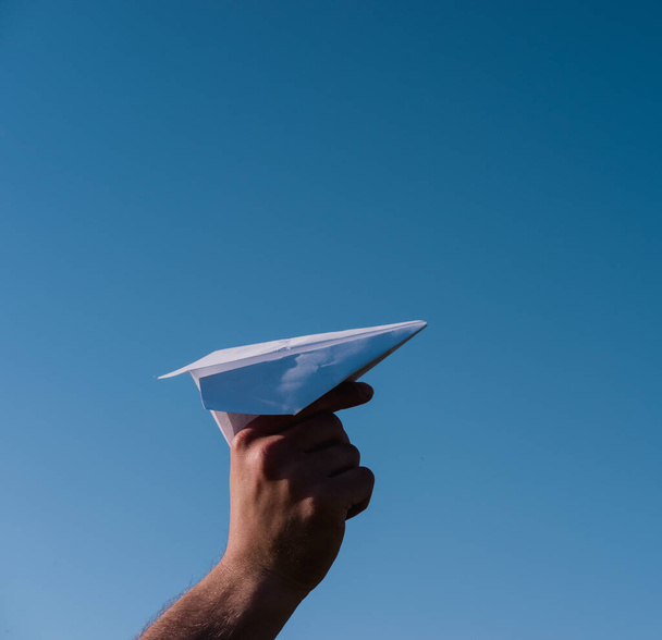 Egy papírrepülőt tartasz a kezedben a kék ég felé. Az origami művészete. Fehér könyv repülőgép. - Fotó, kép