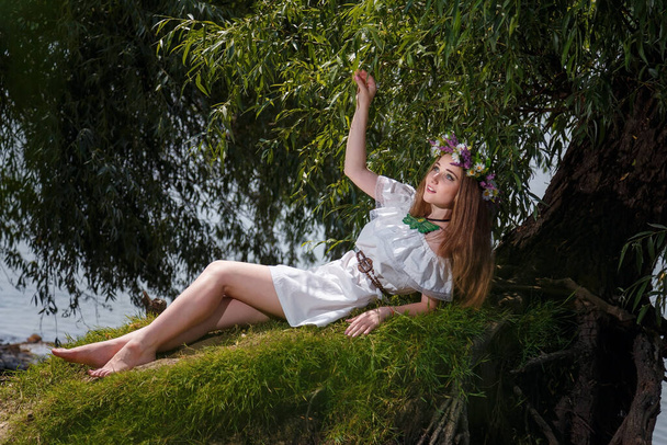Krásná dívka v bílých šatech a květiny věnec na zeleném vrbovém pozadí. 7. července, tradiční slovanský svátek s věšteckými a věšteckými rituály na Ukrajině. - Fotografie, Obrázek