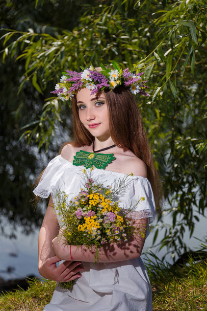 Mooi meisje in witte jurk en krans houden veld bloemen boeket op groene wilg achtergrond. 7 juli, traditionele slavische vakantie met waarzeggerij en waarzeggerij rituelen in Oekraïne. - Foto, afbeelding