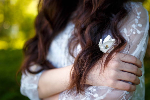 Hands of teenager girl in white dress with flower in her long dark hair in apple garden. Spring blooming and youth concept. - Foto, afbeelding