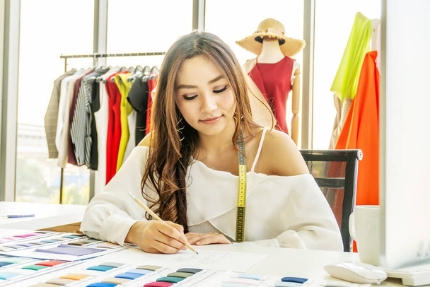 Asian woman designer are thinking and drawing something on paper for customers order items at the designer desk in the studio. Clothes designers are working in the office. Startup designer concept. - Foto, Imagem