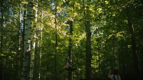 Žena fotící svou dcerku, jak visí na pojistném opasku v lese - zábava v atraktivním parku - Záběry, video