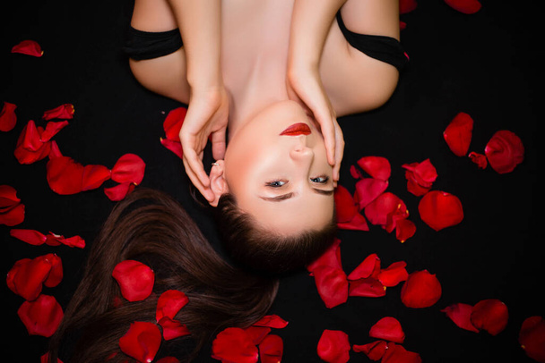 Portrait d'une fille allongée sur un fond noir et pétales de rose. Concept de Saint-Valentin. - Photo, image