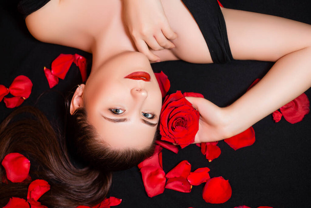 Portrait of a girl lying on a black background and rose petals. Valentine's day concept. - Foto, imagen