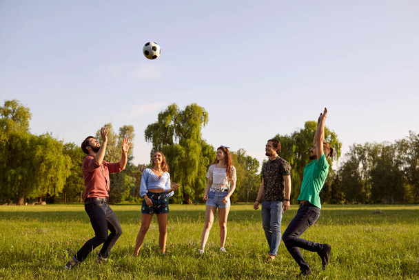 Group of friends having fun playing with a ball on a grass picnic in a summer park. - Zdjęcie, obraz
