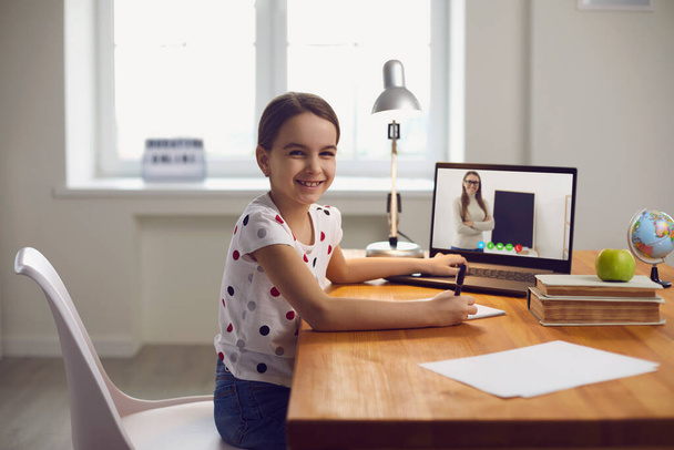 Online video call teaching a child. A little girl doing a lesson watching a video lecture online teacher uses a laptop gadget in the living room. - Φωτογραφία, εικόνα