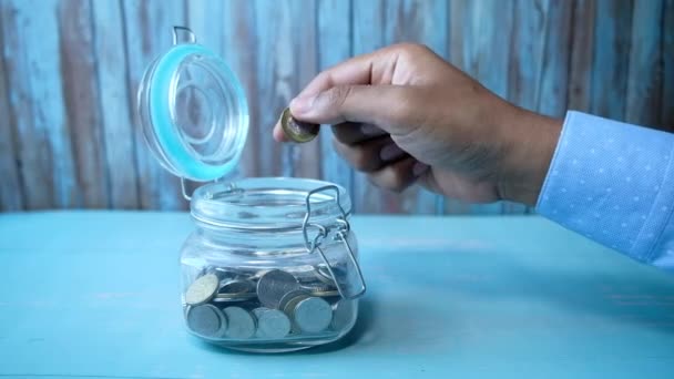Mann schüttet Münzen in Glas auf Tisch. - Filmmaterial, Video