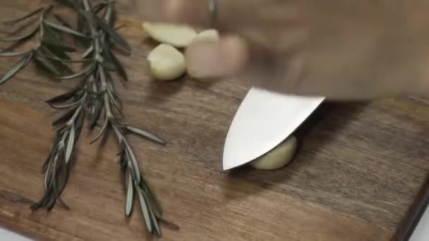 Close up of a woman's hand crushed clove of garlic on a dark brown wooden cutting board with a knife blade.Close up of a woman's hand crushed clove of garlic on a dark brown wooden cutting board with a knife blade. - Footage, Video