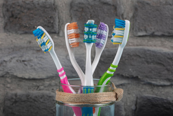 Πολύχρωμες οδοντόβουρτσες σε γυαλί σε μπλε φόντο ξύλου. Έννοια της οδοντιατρικής και στοματικής περίθαλψης. - Φωτογραφία, εικόνα