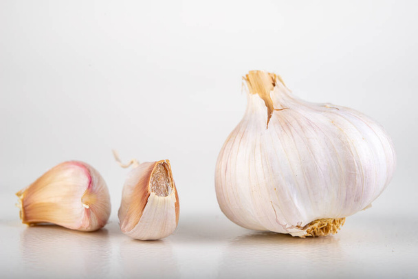 A whole head of garlic and a few cloves of garlic. Vegetables used in home cooking. Light background. - Foto, Bild