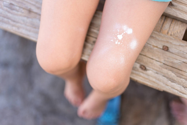 Les jambes des enfants se déploient avec un lait corporel pour la protection solaire. Concept vacances d'été. Concentration sélective. - Photo, image