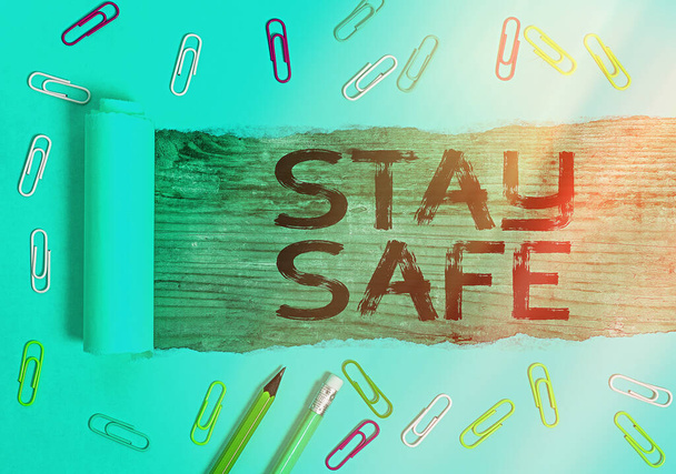 Conceptual hand writing showing Stay Safe. Business photo showcasing secure from threat of danger, harm or place to keep articles Rolled ripped torn cardboard above a wooden classic table. - Photo, Image