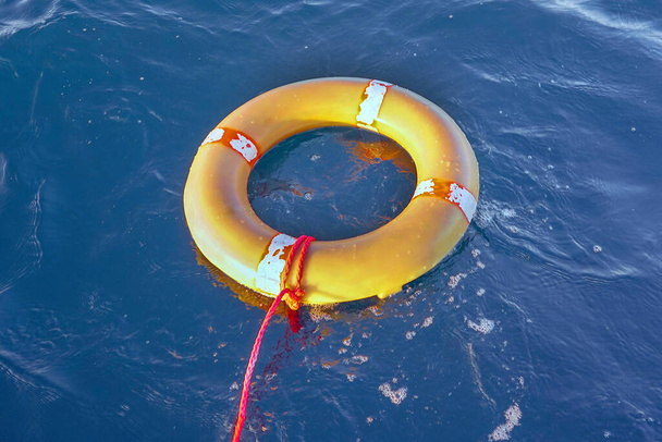 水の上に青い海のロープを持つ黄色の救命艇。生命リングは水の上に浮かんでいます。海にロープを持つ生命リング. - 写真・画像