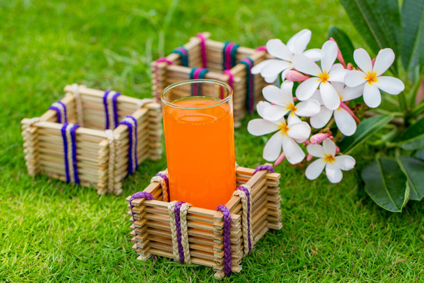 Bambusstäbe Glashalter mit einem Glas Orangensaft auf Gras Hintergrund. - Foto, Bild
