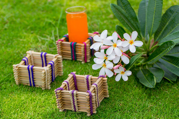 Bamboo sticks glass holder with a glass of orange juice on grass background. - Photo, Image