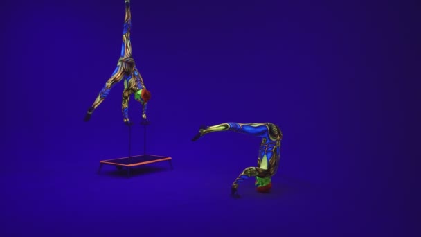Akrobatische Zwillinge in Neon-Kostümen stehen auf Händen und Kopf, auf blauem Zyklorama in ultraviolettem Make-up in fremdem Stil. Leuchtend fluoreszierende Körperkunst leuchtet in der Dunkelheit. - Filmmaterial, Video