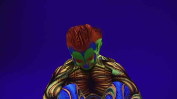 Neon kostümlü akrobatik ikizler kafalarında ve ellerinde, ultraviyole makyajlı mavi siklonamada bir duruş sergileyecekler. Parlak floresan vücut sanatı karanlıkta parlar.. - Video, Çekim