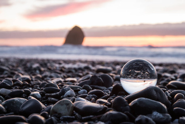 広角レンズで透明なガラス球に逆光した海岸の夕日を背景に少しぼやけたシーンを捉える - 写真・画像
