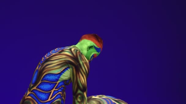 Akrobatická dvojčata v neonovém kostýmu předvádějí stojan na rukou a na hlavě, na modrém cyklorámu v ultrafialovém make-upu v cizím stylu.Světlé fluorescenční těleso září ve tmě. - Záběry, video