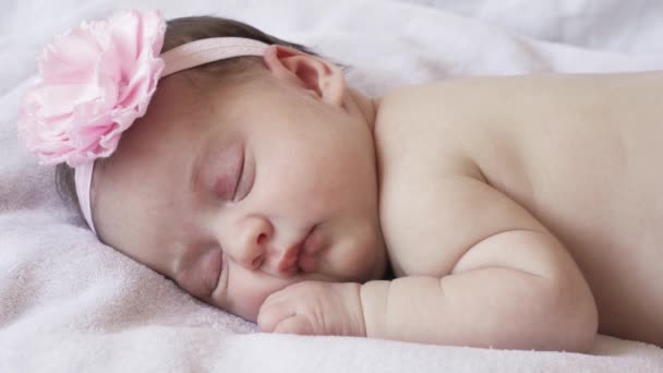 infancy, childhood, development, medicine and health concept - close-up face of a newborn naked sleeping baby girl lying on her stomach with a bandage and a flower on her head on a pink background. - Footage, Video