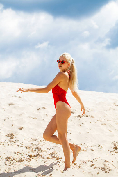 Portrait of a young beautiful girl in a solid red swimsuit posing on the beach - Фото, зображення