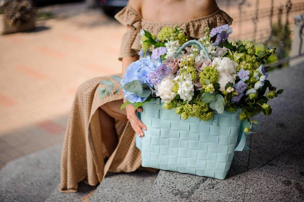 large beautiful blue wicker basket with different flowers of pastel colors stands on the step - Foto, Imagen