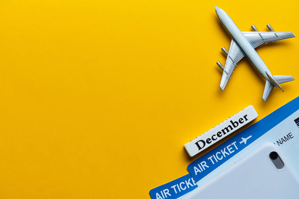コピースペース付き黄色の背景の航空券や飛行機モデルの横にある12月の休暇のコンセプト - 写真・画像
