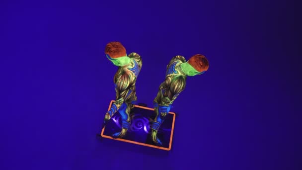 Acrobatische tweeling in neon kostuums om een stand op de handen en het hoofd uit te voeren, op de blauwe cyclorama in ultraviolette make-up in een buitenaardse stijl.Heldere fluorescerende body art gloeit in duisternis. - Video