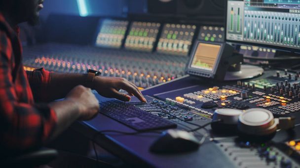 Energetic Male Audio Engineer Producer Working in Music Recording Studio, Mixing Tracks on Control Desk and Software to Create Hit Song Track. Artist Musician Enter His Studio at Sits at Workdesk - Photo, image