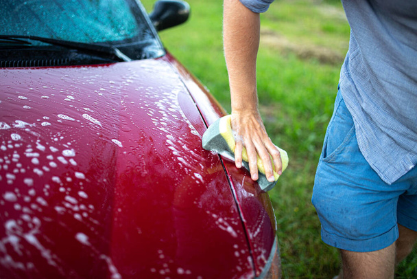 washing a red car with hands, a hook with foam on the back of a car. - Foto, Bild