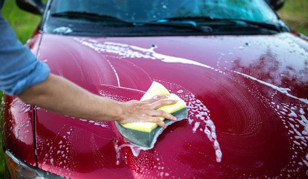 washing a red car with hands, a hook with foam on the back of a car. - Zdjęcie, obraz