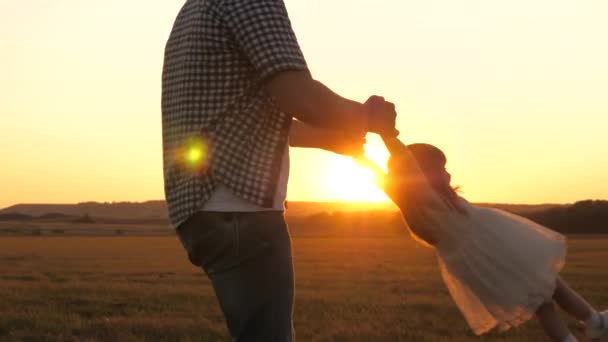 father circles his beloved daughter in arms, a healthy child in flight smiles. child plays fly with dad at sunset in field. dad and baby in the summer park. concept of healthy family and childhood - Footage, Video