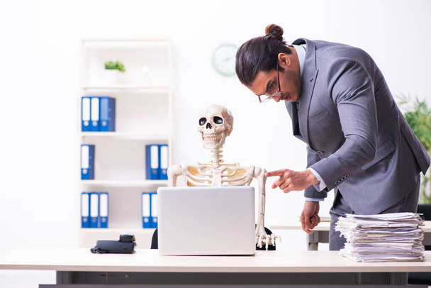 Jovem funcionário masculino e esqueleto no escritório - Foto, Imagem