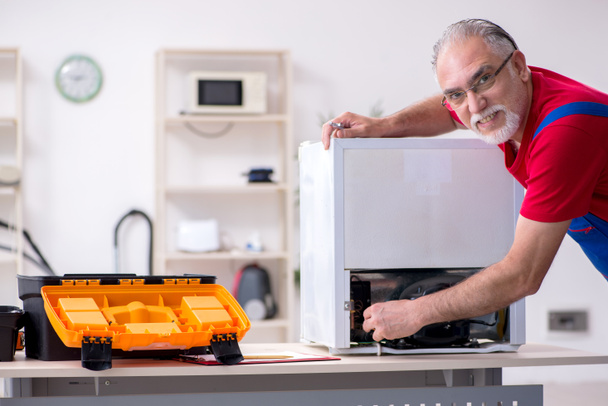 Yaşlı erkek müteahhit içeride buzdolabını tamir ediyor. - Fotoğraf, Görsel