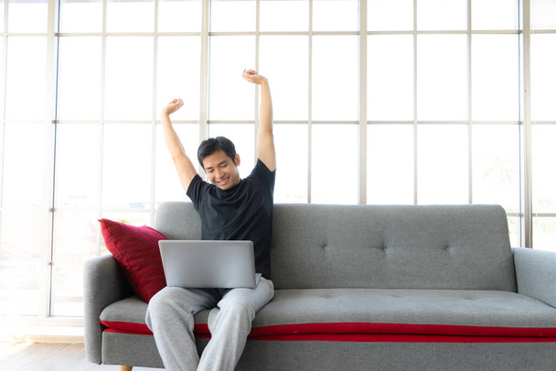 Азиатский человек лениво растягивается, работая с ноутбуком, работая из дома
 - Фото, изображение