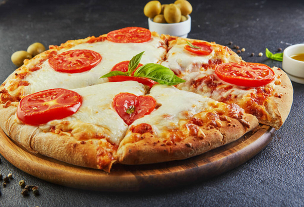 Italian pizza and ingredients for cooking on a black concrete background. Tomatoes, olives, basil and spices. Sliced triangle of pizza. Copy space for text. Side view - Φωτογραφία, εικόνα