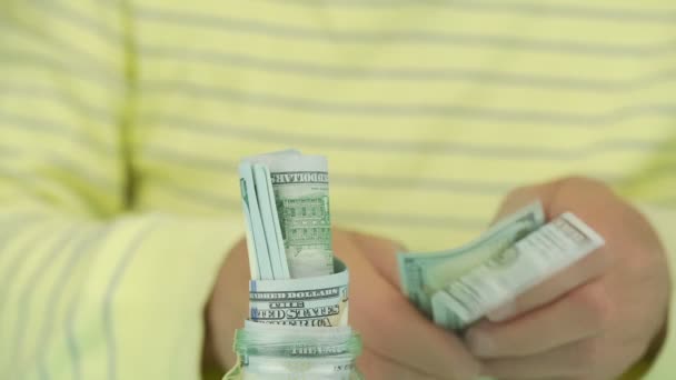 pensioner in pullover rolls dollar banknotes puts into jar - Кадри, відео